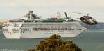 ID 9478 SUN PRINCESS (1999/77441grt/IMO 9000259. Renamed PACIFIC WORLD) sails for Tauranga from the port of Auckland as a helicopter arrives at the Mechanics Bay heliport.